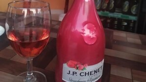 A bottle of J.P. Chenet Strawberry Raspberry wine and a glass of red wine on a wooden table. - Elephant Garden Hotel and Resort (Kanchanrup)