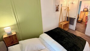 Une chambre à coucher avec un lit, une table de chevet avec une lampe, une commode en bois et une porte.