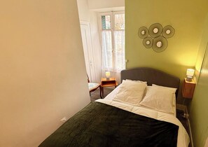 A bedroom with a bed, bedside lamps, a window with curtains, and a wall decoration. - La rabolière Le Mont Dore 3pers (Mont-Dore)