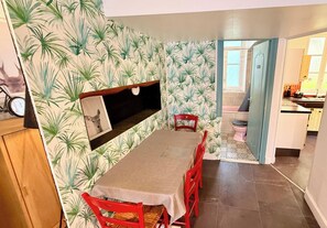 A dining area with a table and chairs, a wall-mounted shelf, and a view into the kitchen. - La rabolière Le Mont Dore 3pers (Mont-Dore)