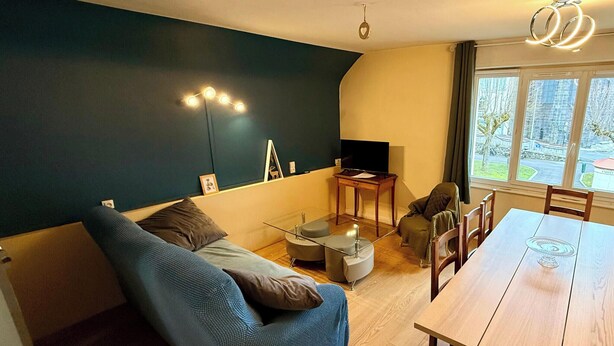 A modern living room with a sofa, a dining table, and a TV. - Le marcassin Le Mont Dore 8pers (Mont-Dore)