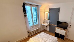 A bedroom with a bed, a window, a radiator, a sink, a mirror, and a TV. - Le marcassin Le Mont Dore 8pers (Mont-Dore)