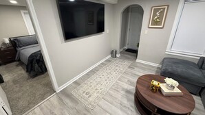 A modern living room with a flat-screen TV, a round coffee table with books and flowers, a gray sofa, and a patterned rug.