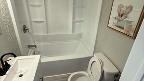 A bathroom with a bathtub, toilet, sink, and a framed picture on the wall.