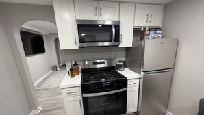 A modern kitchen with white cabinets, a stainless steel microwave, a gas stove, and a refrigerator.