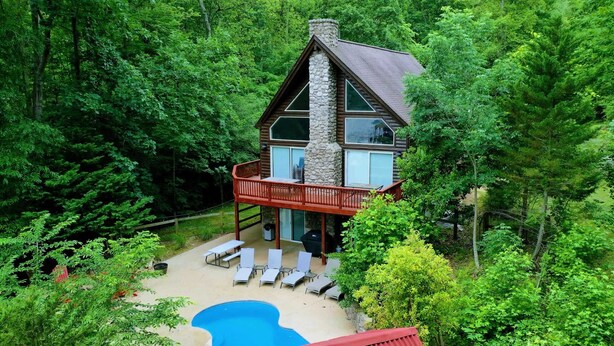 Een chalet met een stenen schoorsteen, een terras met lounge stoelen en een zwembad.