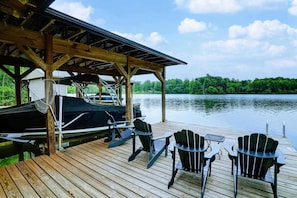 A wooden dock with chairs and a table, a covered area with a boat, and a lake view. - Lakefront A-Frame | Private Pool, Beach & Dock! (Bumpass)