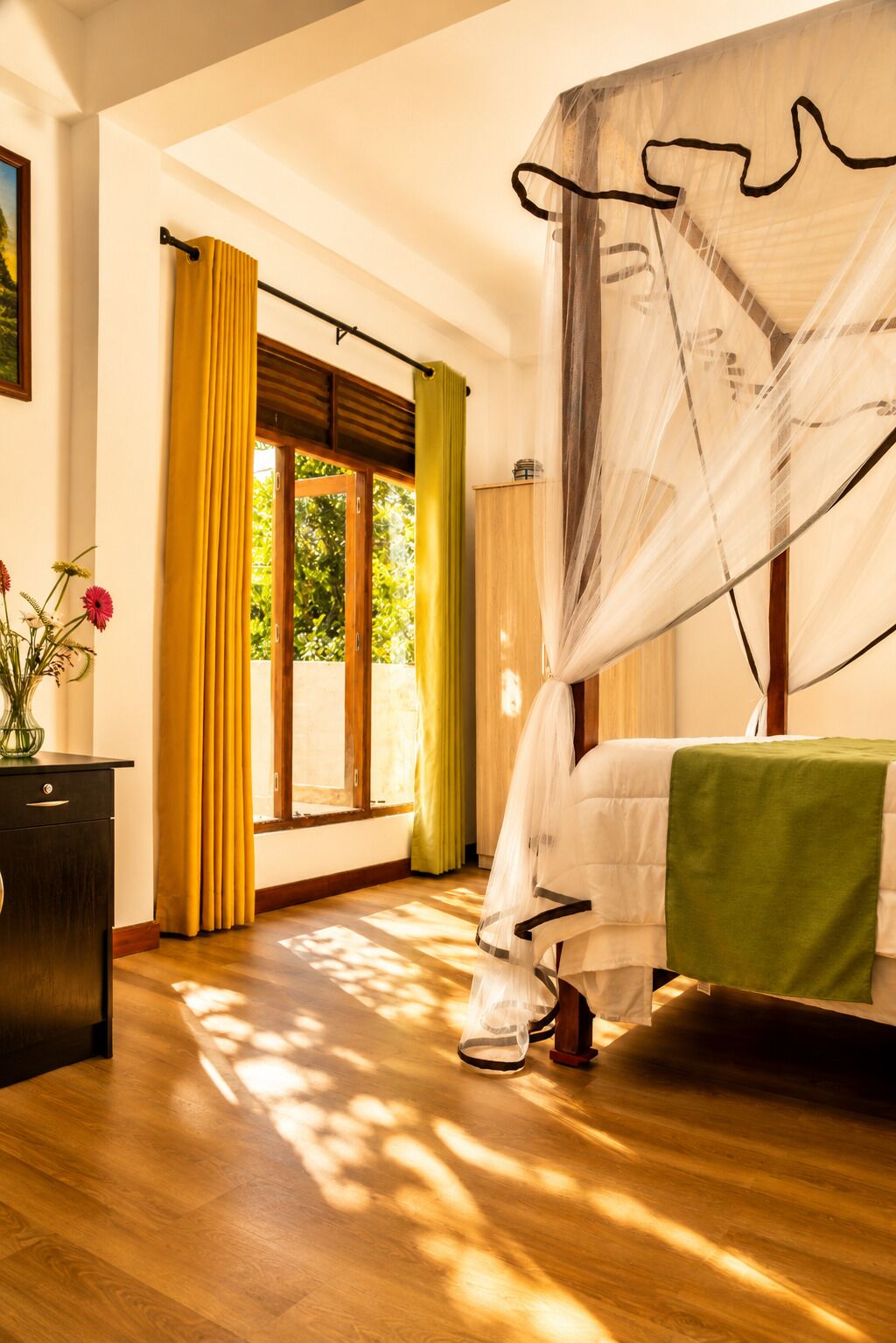 Un dormitorio con cama con dosel, suelo de madera y ventana con cortinas.
