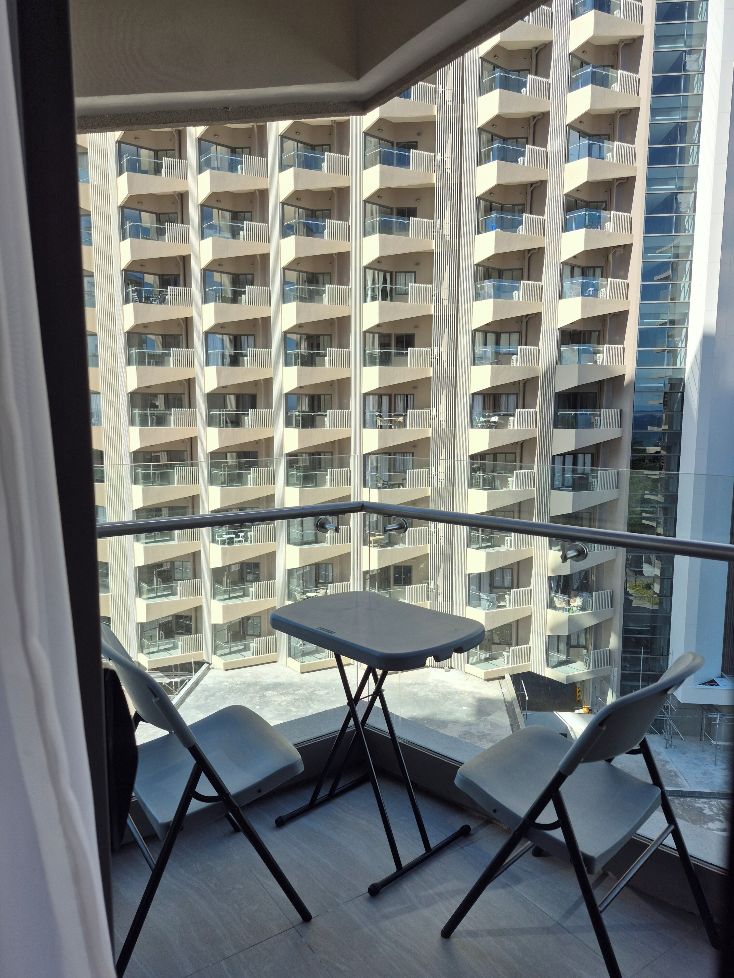 Un balcon avec une table et des chaises, donnant sur un immeuble de grande hauteur doté de nombreux balcons.