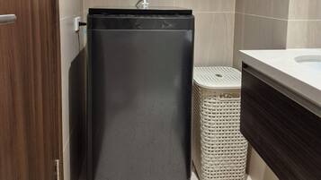 A compact bathroom with a small, dark-colored washing machine, a white laundry basket, and a modern sink.