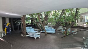 Un espace de détente intérieur avec des canapés et des tables bleus, entouré d’arbres.