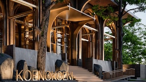 A modern building with arched structures, a staircase leading to the entrance, and a tree in the foreground.