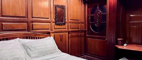 A hotel room with a wooden paneled wall, a bed with white linens, a round mirror, and a small table with a lamp.