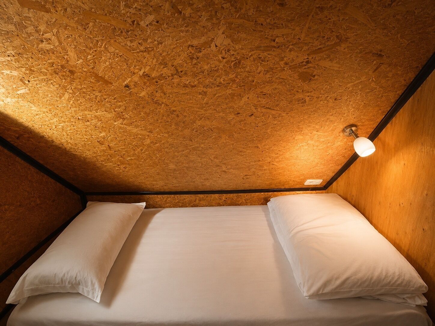 A single bed with white bedding in a room with wooden walls and a sloped ceiling.