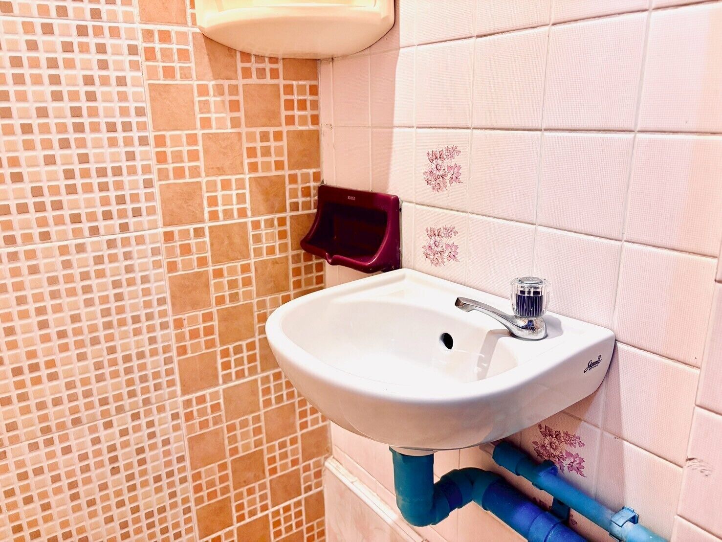 Un baño con un lavamanos blanco, un jabonera roja y una pared de azulejos con un estampado floral.