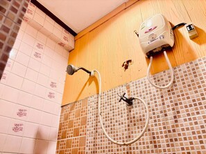 A shower area with a handheld showerhead, a wall-mounted water heater, and a tiled wall with floral patterns. - Sukhum Ban Songthai (Bangkok)