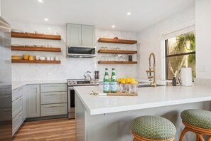 A modern kitchen with a central island, wooden shelves, and a large window. - Kapalua Ridge | Ocean View 2 BR, Sleeps 8 | Car Incl. w/ 6+ Nights | KRV ML-3942 by KBM (Lahaina)