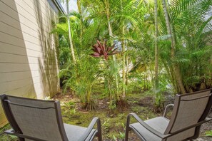 A patio with two chairs, surrounded by lush tropical plants and a building wall. - Kapalua Ridge | Ocean View 2 BR, Sleeps 8 | Car Incl. w/ 6+ Nights | KRV ML-3942 by KBM (Lahaina)