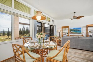 A dining area with a round table, wicker chairs, and a hanging light fixture. - Kapalua Ridge | Ocean View 2 BR, Sleeps 8 | Car Incl. w/ 6+ Nights | KRV ML-3942 by KBM (Lahaina)