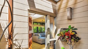 A modern interior with a glass door leading to a living area, a potted plant, and a wall-mounted light fixture. - Kapalua Ridge | Ocean View 3 BR, Sleeps 12 | Car Incl. w/ 6+ Nights | KRV ML-3963 by KBM (Lahaina)