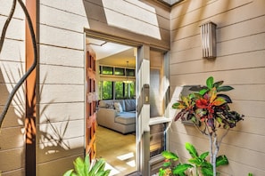 A modern interior with a glass door leading to a living area, a potted plant, and a wall-mounted light fixture. - Kapalua Ridge | Ocean View 3 BR, Sleeps 12 | Car Incl. w/ 6+ Nights | KRV ML-3963 by KBM (Lahaina)