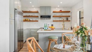 A modern kitchen with grey cabinets, a central island, and wooden stools. - Kapalua Ridge | Ocean View 3 BR, Sleeps 12 | Car Incl. w/ 6+ Nights | KRV ML-3963 by KBM (Lahaina)