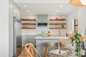 A modern kitchen with grey cabinets, a central island, and wooden stools. - Kapalua Ridge | Ocean View 3 BR, Sleeps 12 | Car Incl. w/ 6+ Nights | KRV ML-3963 by KBM (Lahaina)