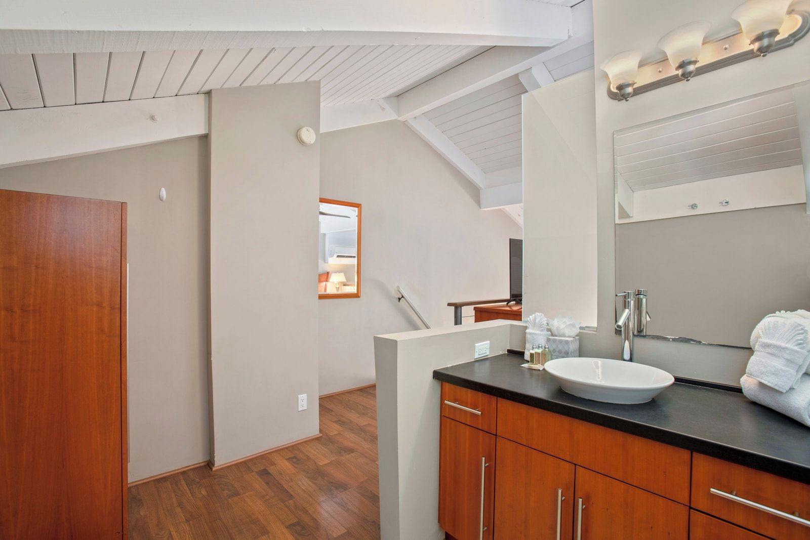 A modern bathroom with a wooden vanity, a large mirror, and a ceiling fan.