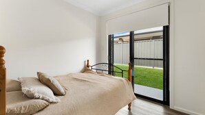 Un dormitorio con cama, almohadas, una ventana y vista a un patio trasero.