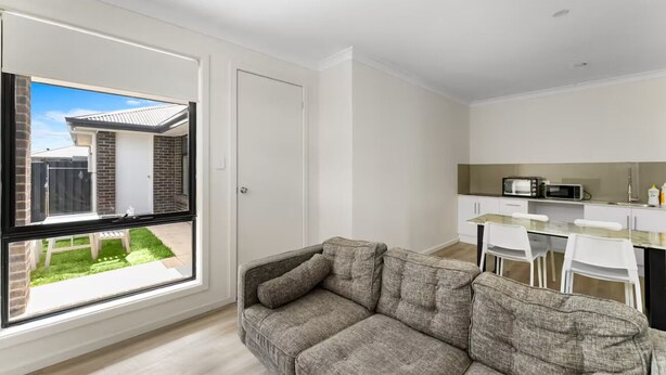 Un apartamento moderno con un sofá gris, una cocina con armarios blancos y vista a un patio trasero.