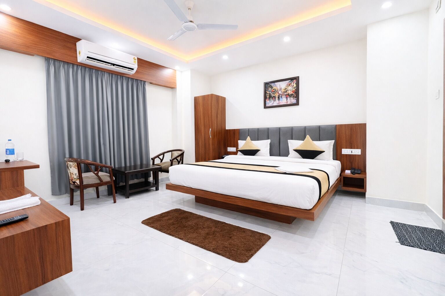 Una habitación de hotel moderna con cama, escritorio, silla, aire acondicionado y un cuadro en la pared.