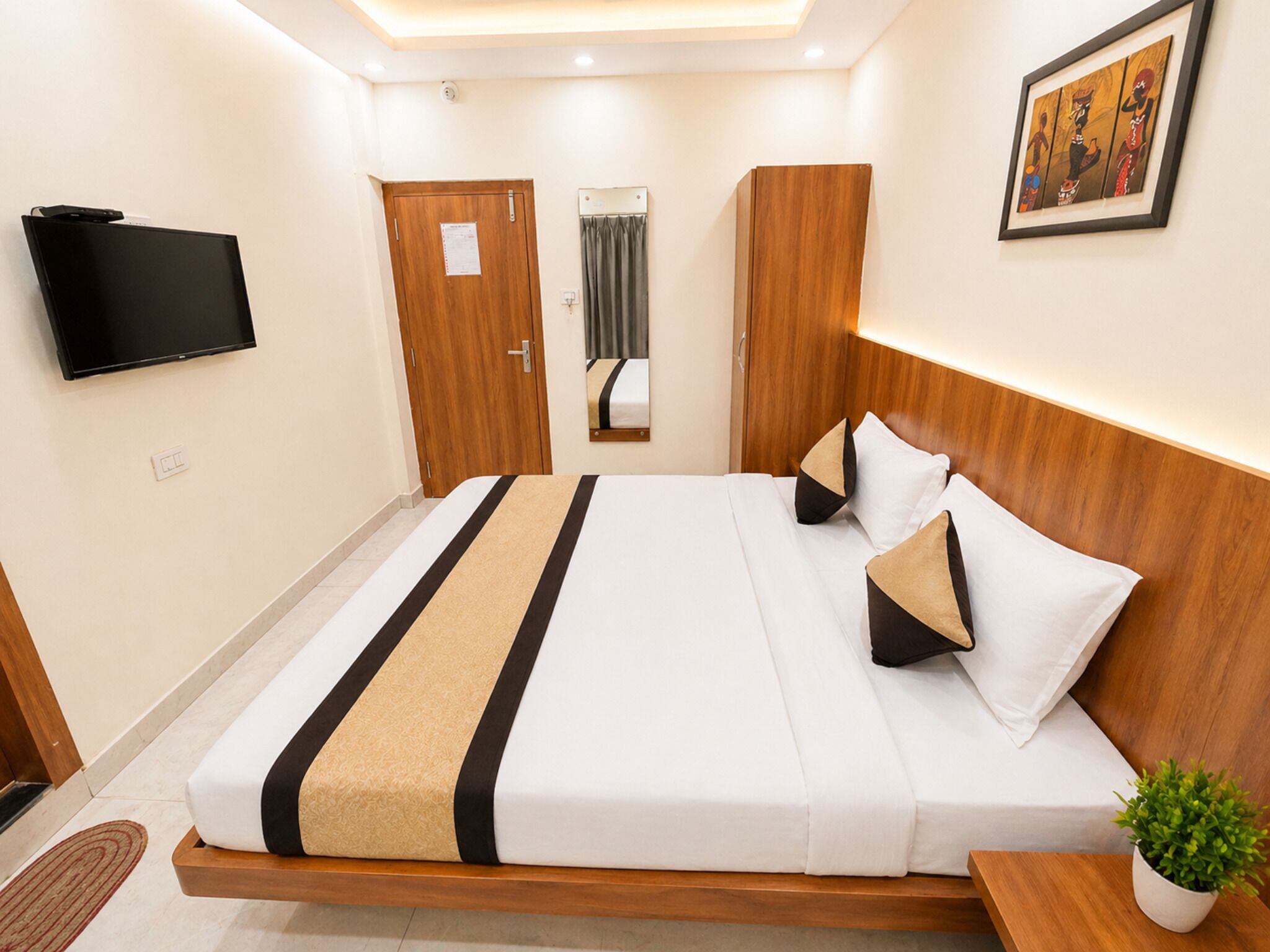 Ein Hotelzimmer mit einem Bett, einem Fernseher, einer Tür, einem Spiegel und einem gerahmten Bild an der Wand.