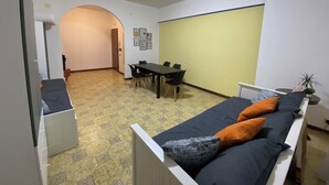 Pieni huone, jossa on sänky, pieni pöytä ja tuoleja. Huoneesta on ovi toiseen huoneeseen.