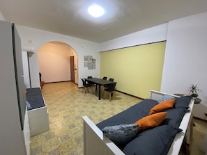 Ein kleines Zimmer mit einem Bett, einem Tisch und Stühlen. Eine Tür führt in einen weiteren Raum.