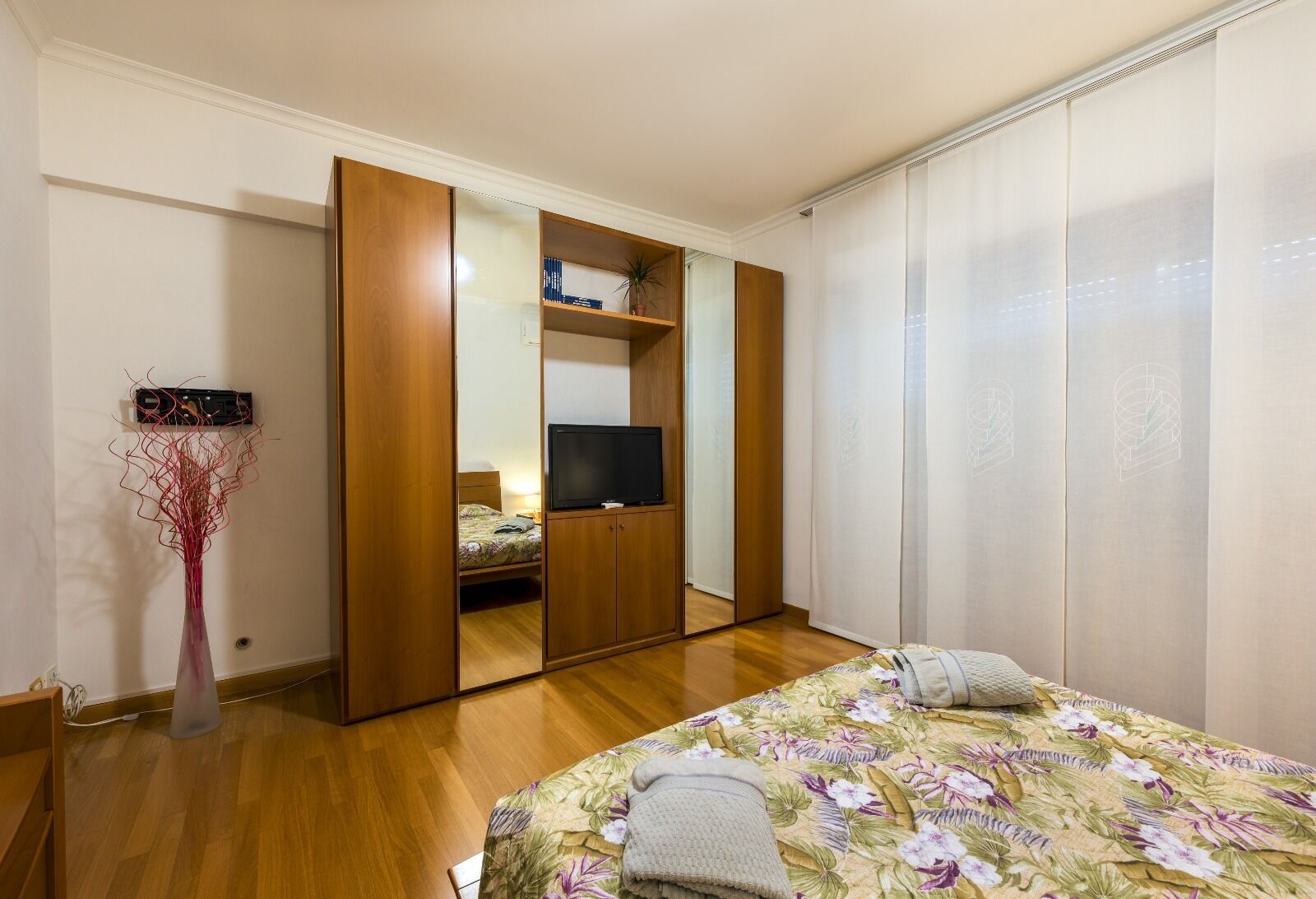Ein Schlafzimmer mit Bett, Kleiderschrank, Fernseher und einer Zimmerpflanze.