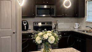 A kitchen with dark cabinets, a stainless steel microwave, a coffee maker, and a vase with flowers on the counter.