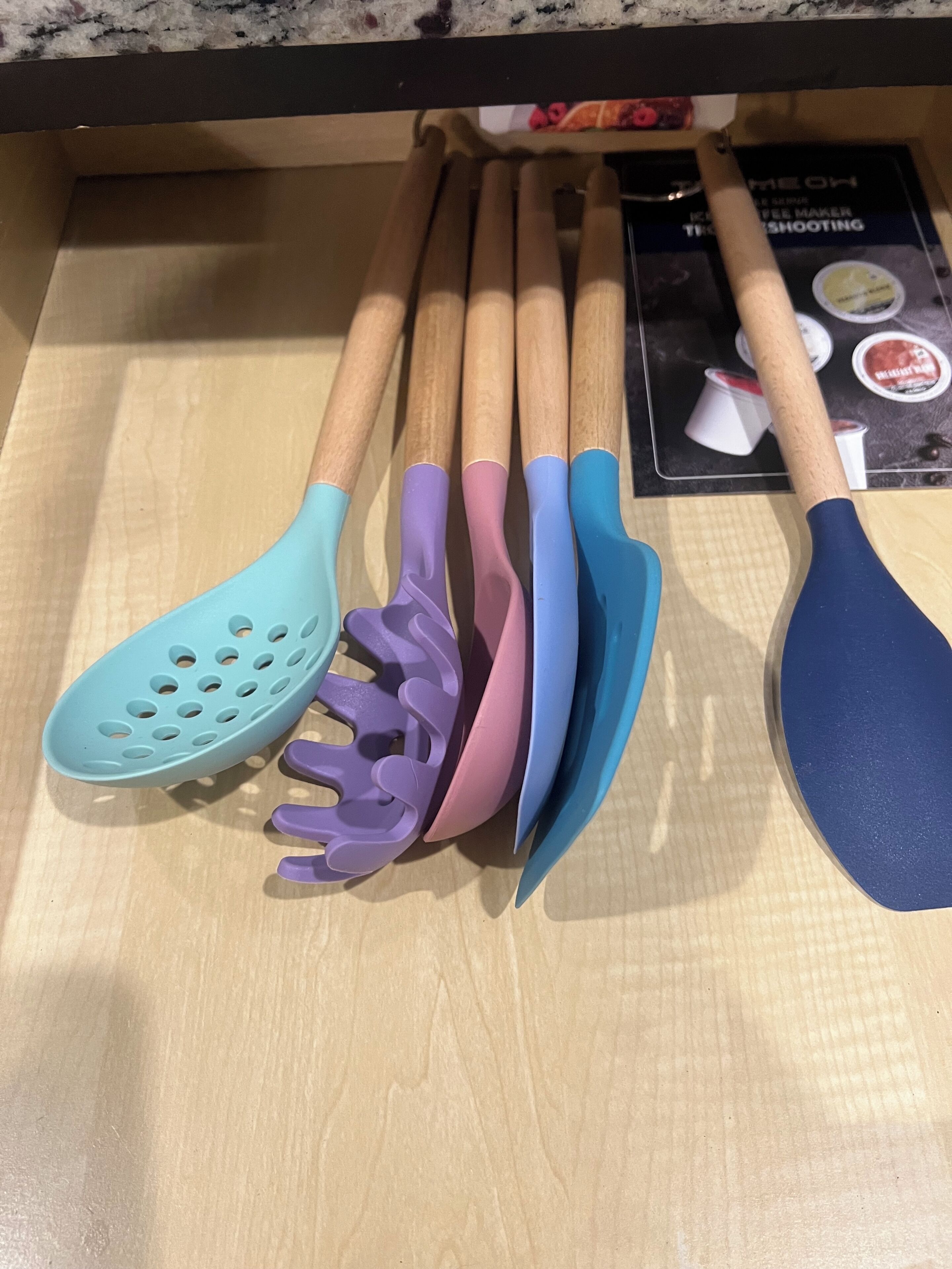 A kitchen utensil drawer with wooden handles and plastic spouts in various colors.
