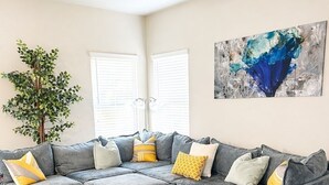Un canapé modulable avec plusieurs coussins, un ventilateur de plafond, un grand tableau abstrait et une plante en pot.