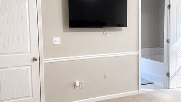 A room with a flat-screen TV mounted on the wall, a white door, and a carpeted floor.