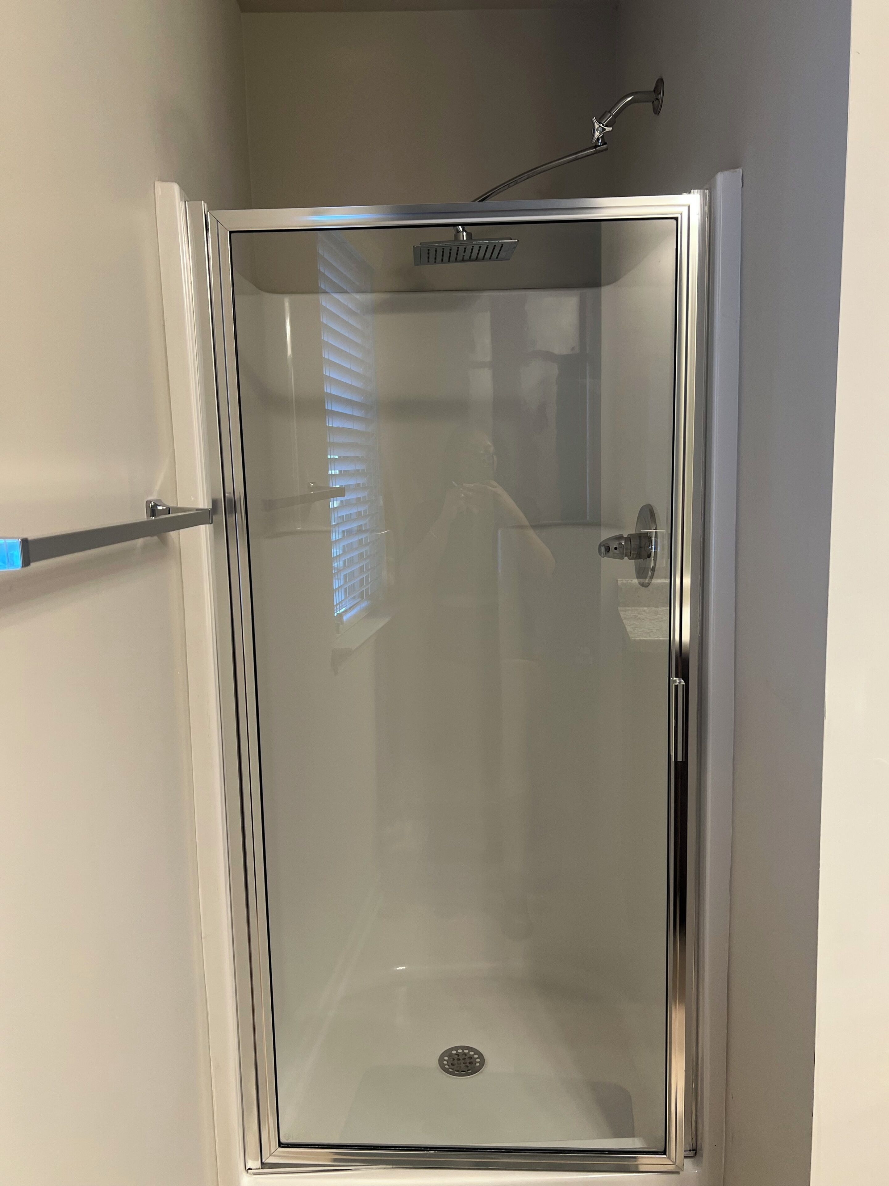 Une cabine de douche fermée par des parois en verre, équipée d’un pommeau de douche, d’une barre d’appui et d’un drain.