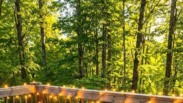 A deck with a sofa and a table, surrounded by a wooden railing and string lights.