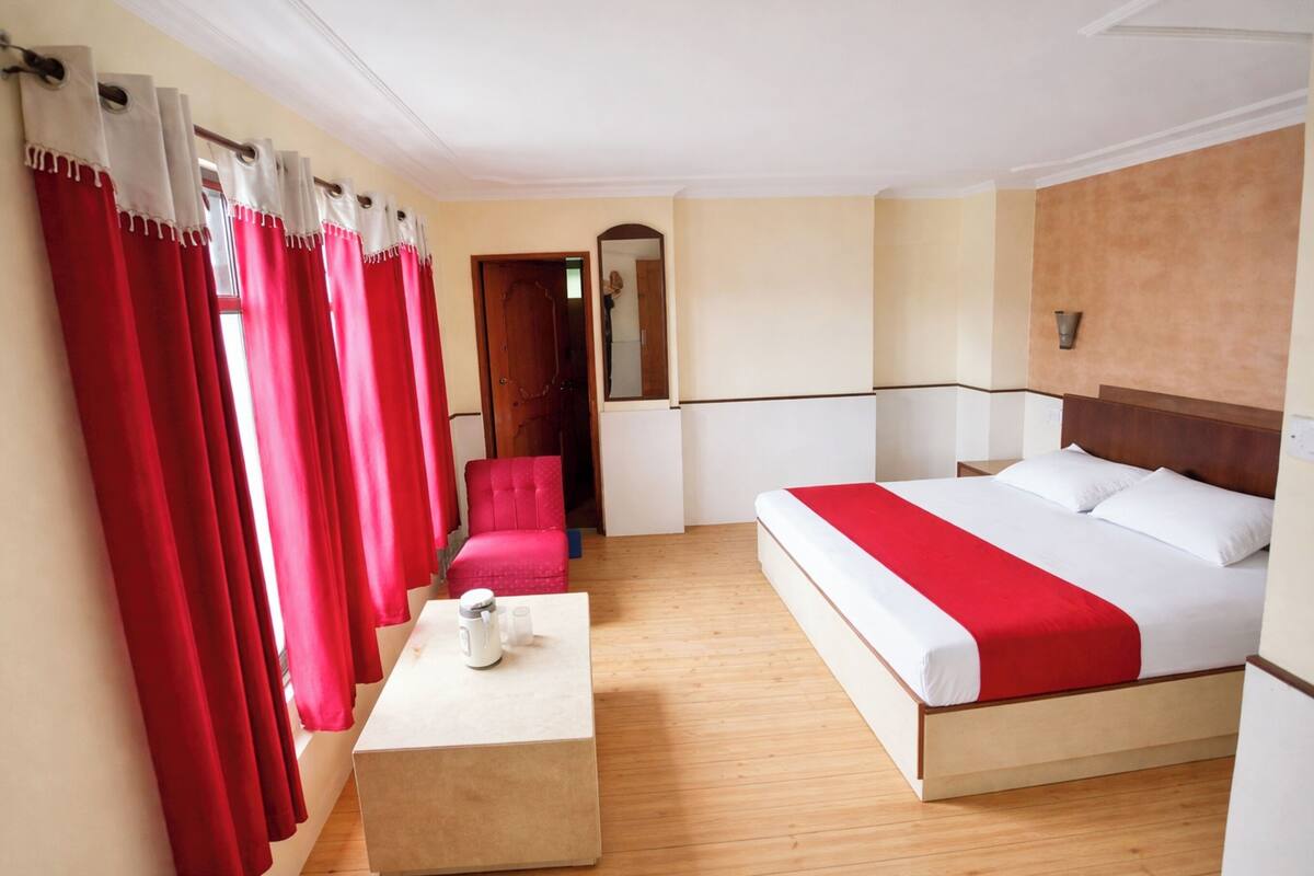 Una habitación de hotel con una cama, una silla, una mesa con hervidor y cortinas rojas.