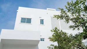 Um edifício moderno branco com teto plano, duas janelas visíveis e uma seção com fachada perfurada.