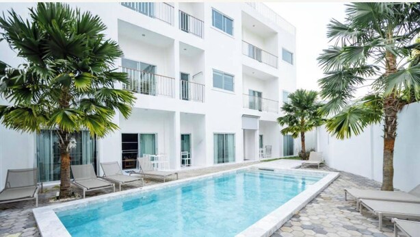 Um edifício moderno com piscina, palmeiras e espreguiçadeiras.