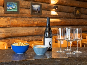 Una mesa de madera rústica con una botella de vino, dos cuencos de aperitivos y tres copas de vino.