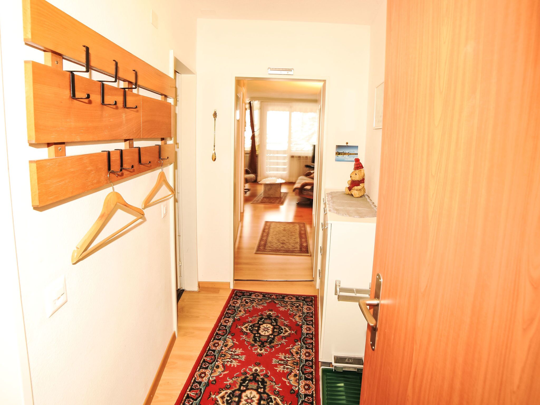 A hallway with a wooden coat rack, a red patterned rug, and a white cabinet with a teddy bear on top.