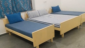 Deux lits simples avec des cadres en bois et des matelas bleus, un oreiller à rayures et un rideau bleu.