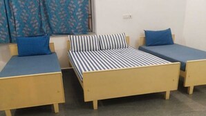 Une chambre avec deux lits simples, une petite table et un rideau.