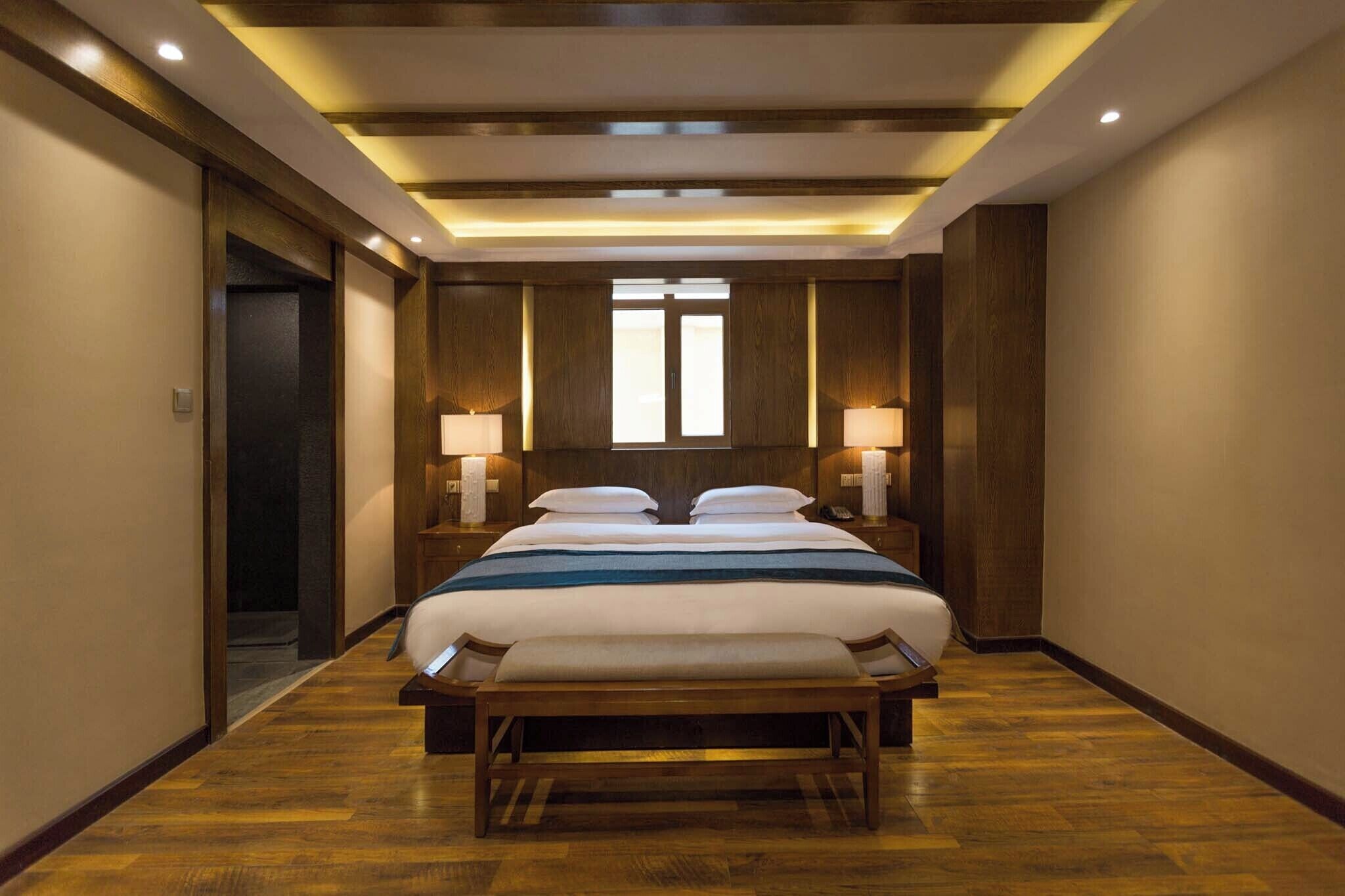 A hotel room with a large bed, bedside lamps, a bench, and a wooden floor.
