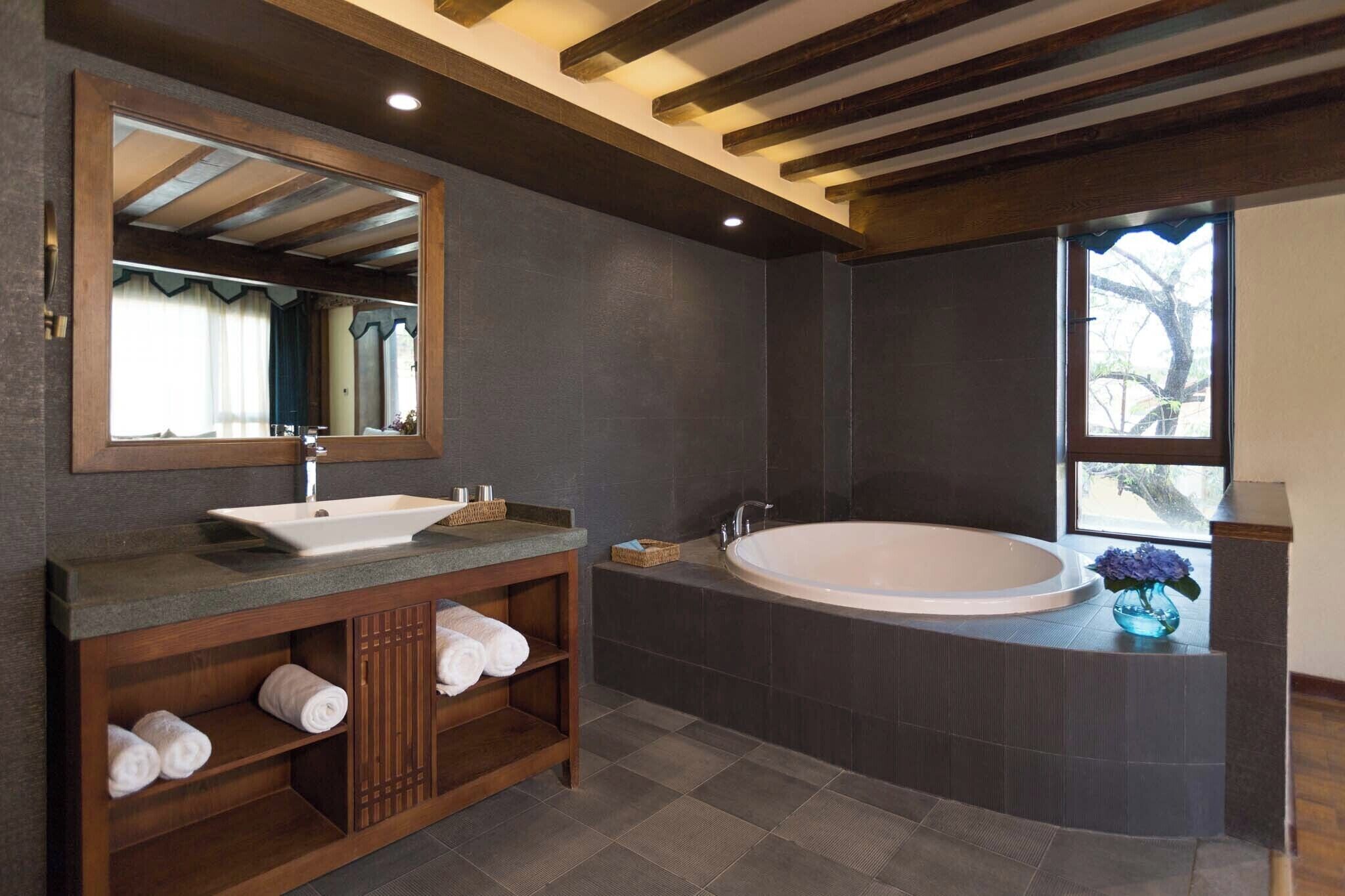 Un baño moderno con una bañera grande, un tocador con lavabo, un espejo y una ventana que aporta luz natural.
